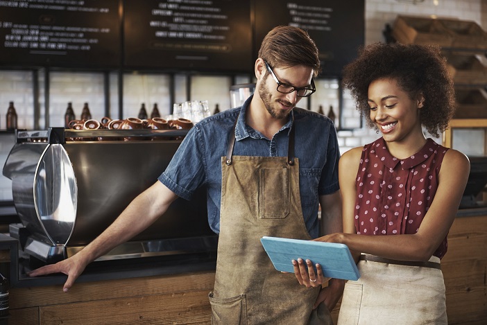 Shot of a smiling woman and man standing inside a coffee shop looking at something on their touchscreen